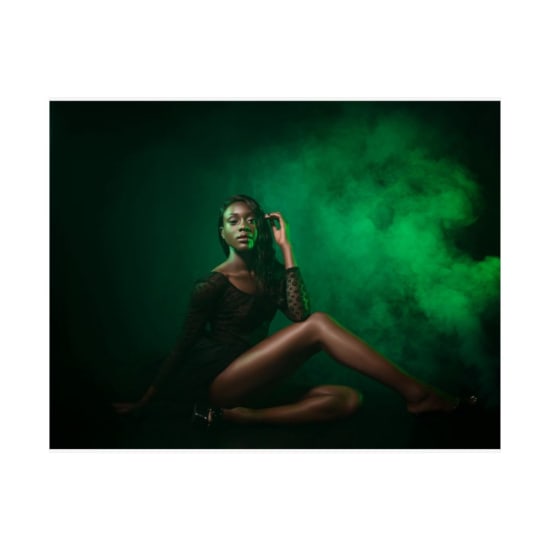 African American model posing gracefully against a dramatic green smoke backdrop. Fashion and style concept.