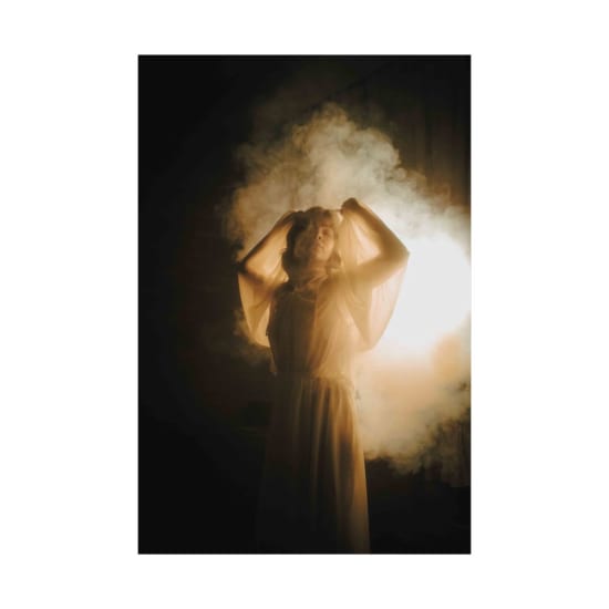 A woman enveloped in mist, illuminated by soft, warm lighting, creating an ethereal atmosphere.