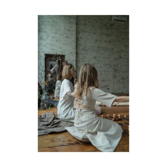 Two women in white dresses meditating indoors with candles and serene ambiance.