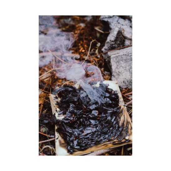 Close-up of a burning sheet of paper emitting smoke outdoors.