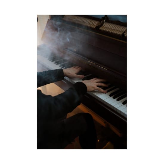 Hands gracefully play a grand piano surrounded by a mysterious smoky atmosphere.