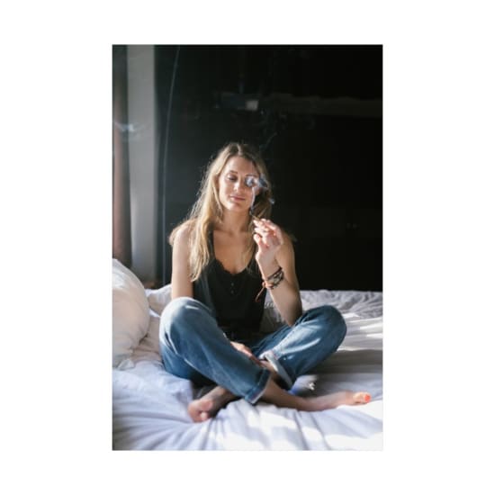A young woman enjoying cannabis relaxation while sitting on a bed indoors.
