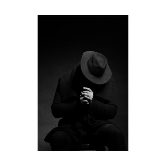 Moody black and white photo of an anonymous person in a hat with folded hands.