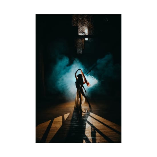 A mesmerizing silhouette of a dancer posing with colorful smoke on a stage.