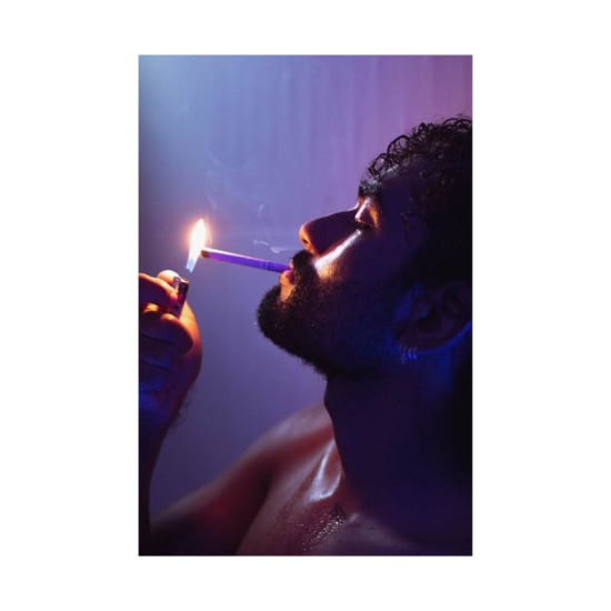 Dramatic neon-lit close-up of a bearded man lighting a cigarette, creating an intense atmosphere.