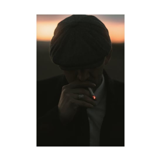A silhouette of a man smoking a cigarette against a dramatic sunset background.
