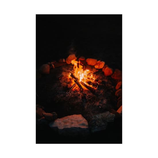 Warm campfire glowing in the dark, surrounded by rocks in a serene outdoor setting.