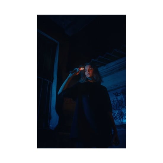 Artistic portrait of a woman holding a lit matchstick in a dark urban environment.