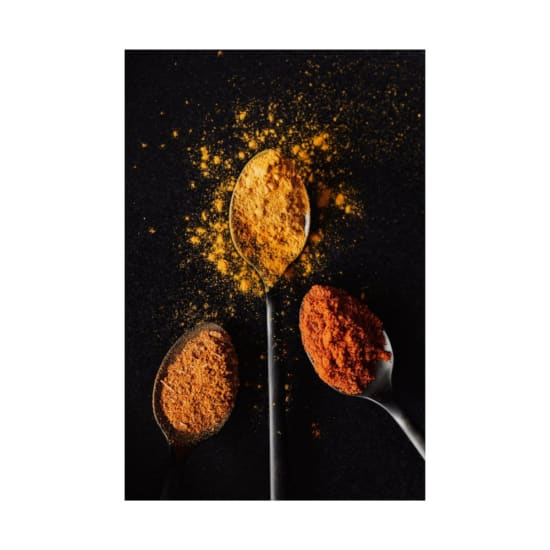 Vivid spices in spoons on black background, showcasing turmeric, paprika, and chili powder.