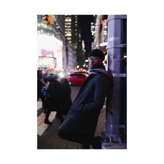 Stylish man posing on a busy city street at night with colorful lights.