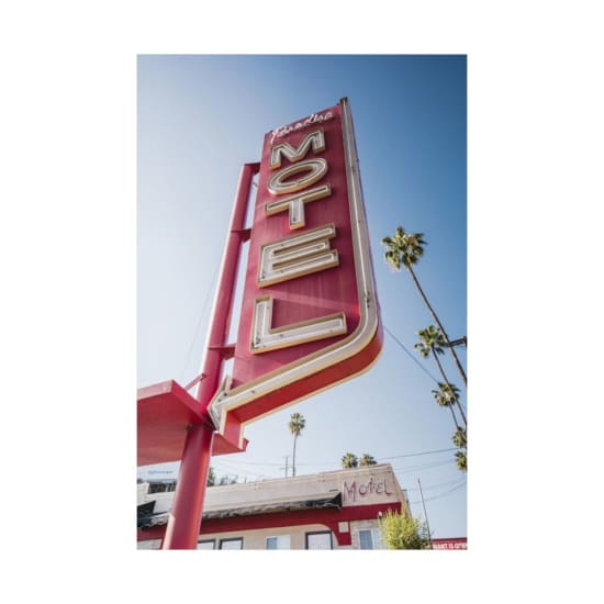 Vintage motel sign in Los Angeles with palm trees under a clear blue sky.