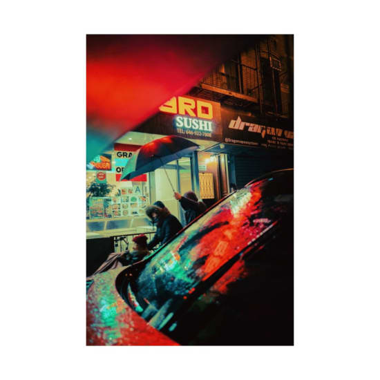 Colorful city street scene at night with people walking under umbrella, reflecting neon lights.