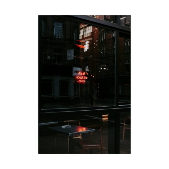 Moody urban cafe scene with neon reflections in a glass facade, exuding a warm ambiance.