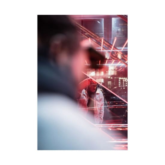 A young adult reflected in glass amidst vibrant neon city lights at night.