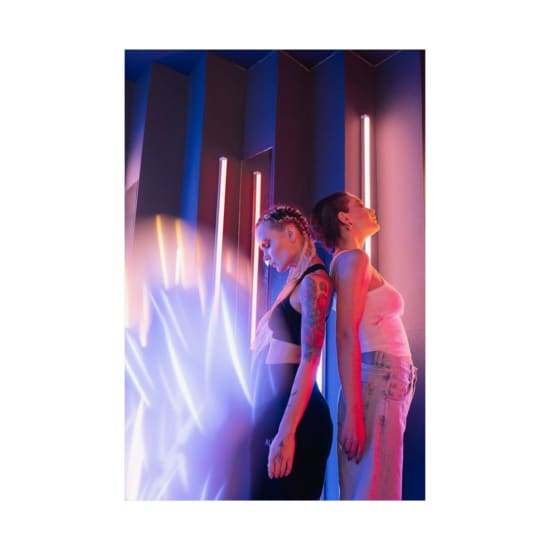 Two women back to back with neon glow in artistic portrait, showcasing creative makeup.