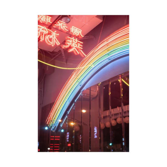 Colorful neon rainbow in an urban setting, illuminating a dim night street with vibrant light.