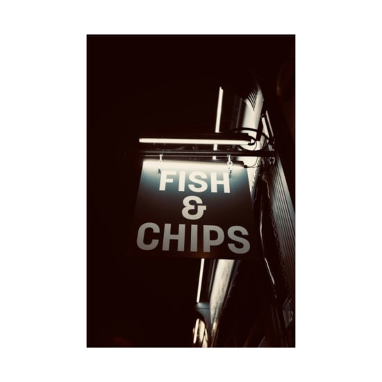 Illuminated fish and chips sign glowing in London's night streetscape.