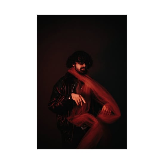 A stylish man poses with a red scarf against a moody backdrop, embodying modern fashion.