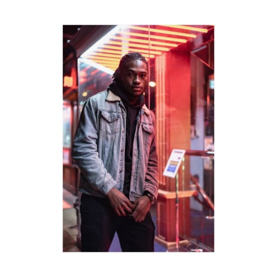 Stylish African American man in a denim jacket posing confidently in an urban setting at night.