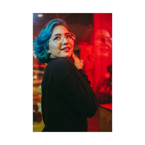 Colorful portrait of a woman with blue hair reflecting in glass at night.