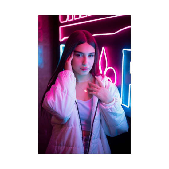 Stylish portrait of a young woman in white jacket under vibrant neon lights.