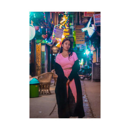 A stylish woman poses in a lively night bazaar adorned with colorful lights and signs.