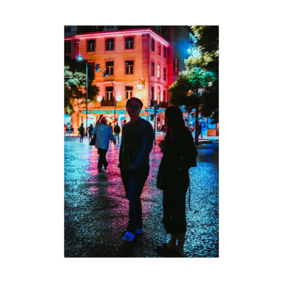 Colorful night scene in Lisbon with people walking under neon lights and illuminated buildings.
