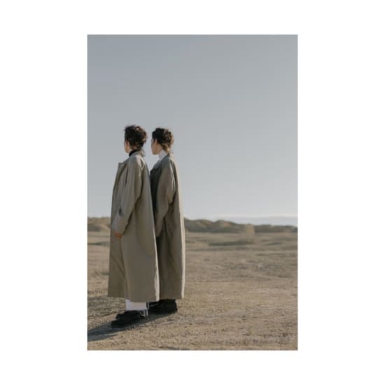 Two women in trench coats standing in a desert setting, depicting fashion and style.