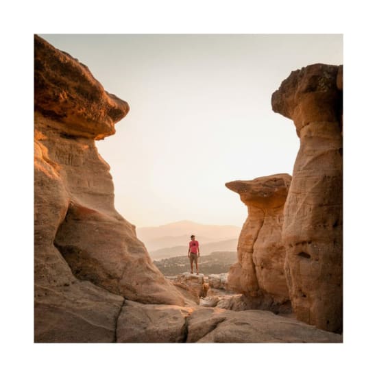 Hiker stands between scenic rock formations at sunset in Colorado Springs.