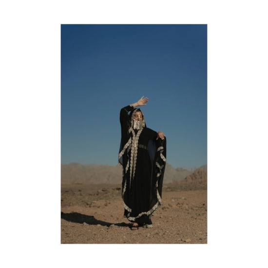 Woman in a traditional black gown and headscarf posing elegantly in a desert landscape.