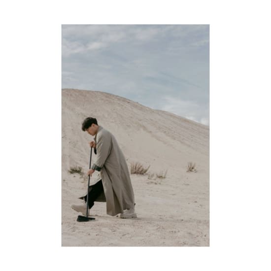 Unusual scene of a man sweeping sand in a vast desert landscape under clear skies.