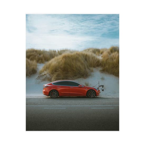 A sleek red electric car parked by sandy dunes under a blue sky, showcasing modern transportation in a natural landscape.