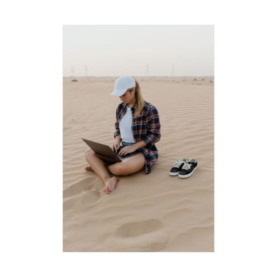 Young woman sitting on sand using a laptop. Digital nomad lifestyle in a desert environment.