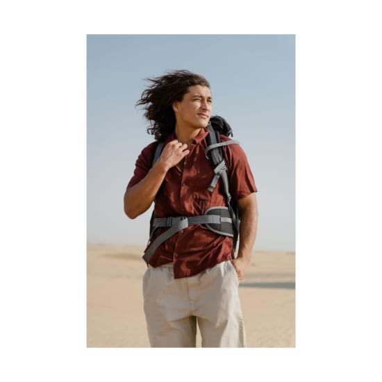 A young male traveler with long hair stands confidently in a vast desert, exuding adventure.