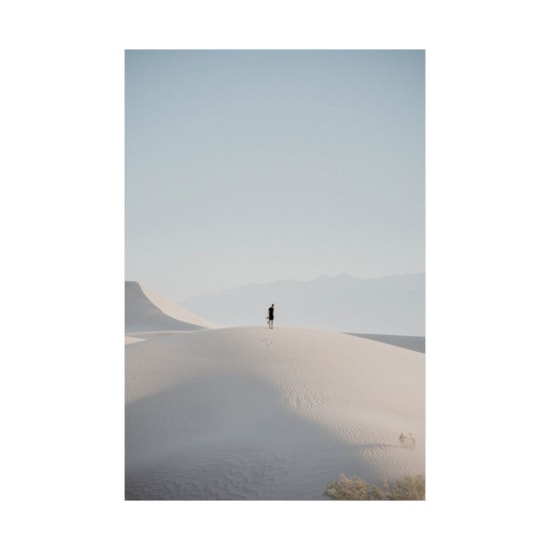 A lone person stands on a vast sand dune under a clear blue sky, embodying solitude and nature's grandeur.