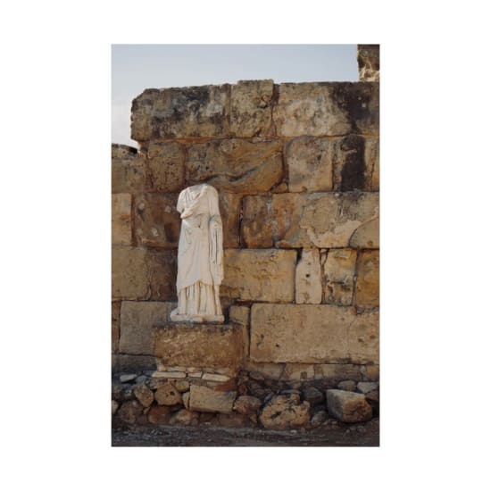 An ancient statue in Kıbrıs stands against a historic stone wall.
