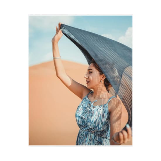 Elegant woman in a blue dress holding a scarf in a sunny desert landscape.