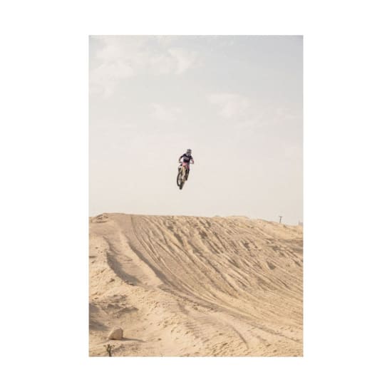 Dramatic capture of a motocross rider in mid-air over a sandy desert track.