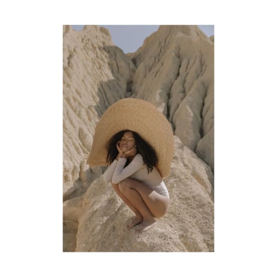 Stylish woman in a large straw hat posing elegantly on a rocky desert terrain.
