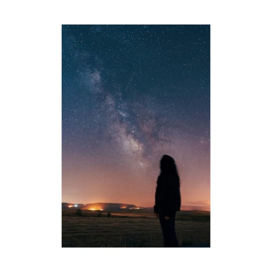 Silhouette of a woman gazing at the Milky Way in a rural starry night.