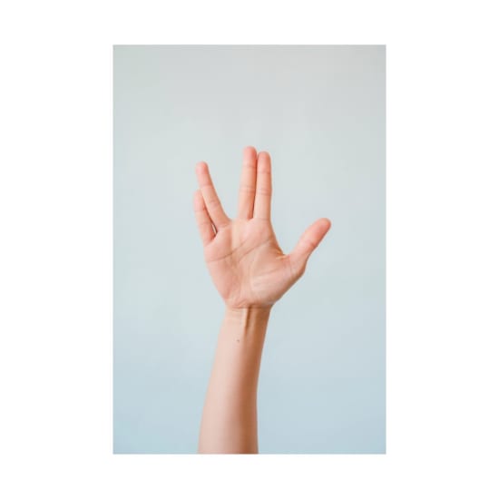 Close-up of a human hand making the Vulcan salute on a light background.