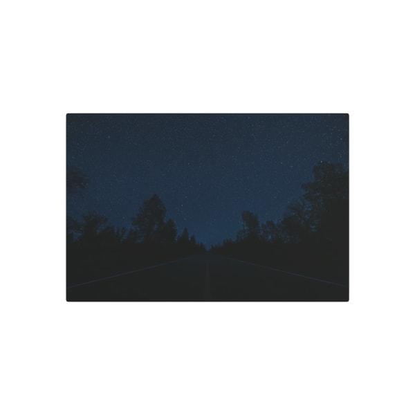A tranquil starry sky above a silhouetted forest flanking an empty road at night.