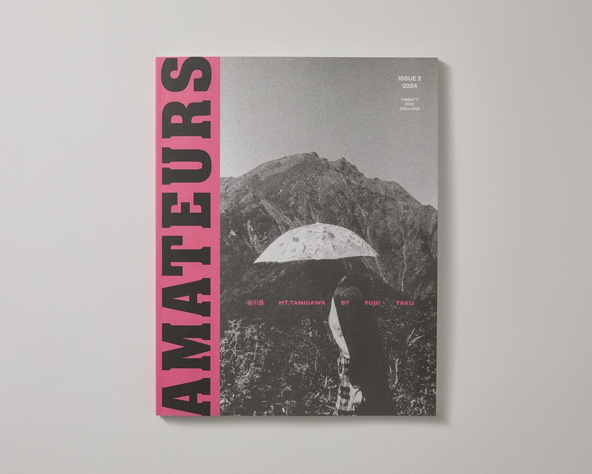A magazine cover with the word "AMATEURS" in large pink letters on the left, features a black and white image of a person holding an umbrella in front of a mountainous landscape.