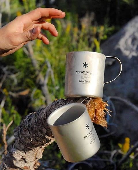 Two titanium Snow Peak cups sit in the snow, with a fuel canister positioned in the background.