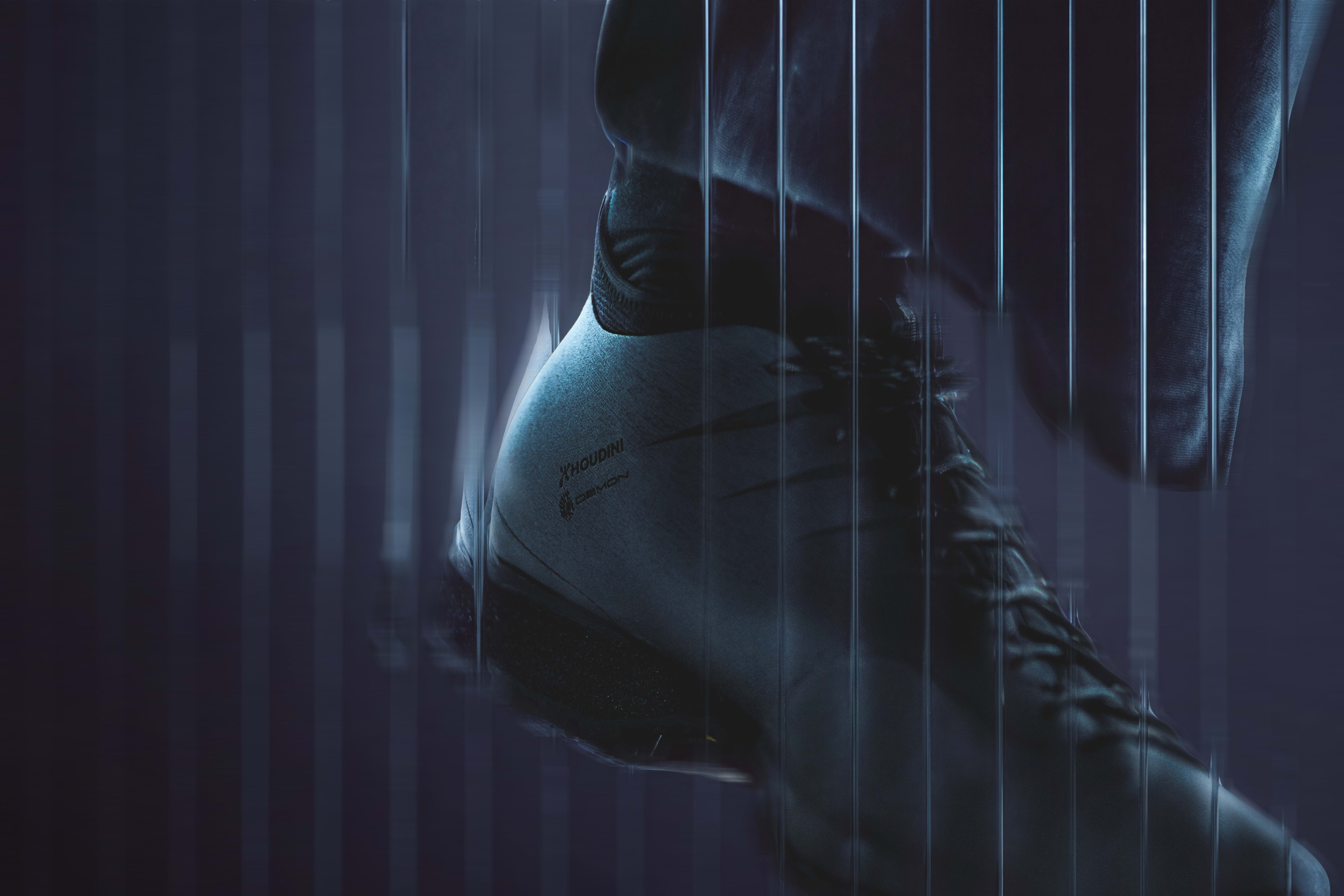 A close-up of a sleek, dark athletic shoe and leg positioned against a moody, dark blue background with vertical light streaks.