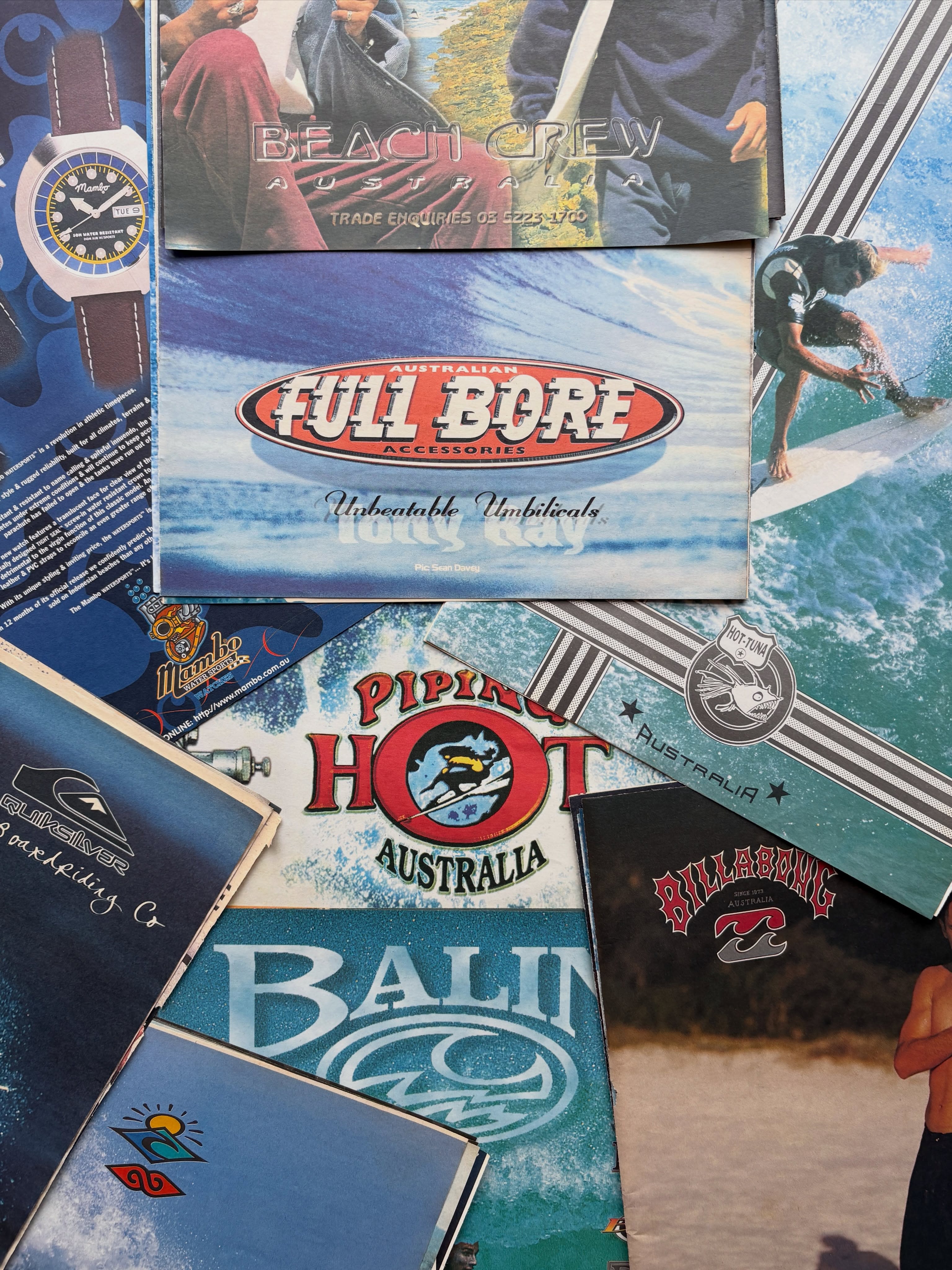 A collection of colorful surf-themed brochures and magazines fills the foreground, layered over a background of more printed materials.