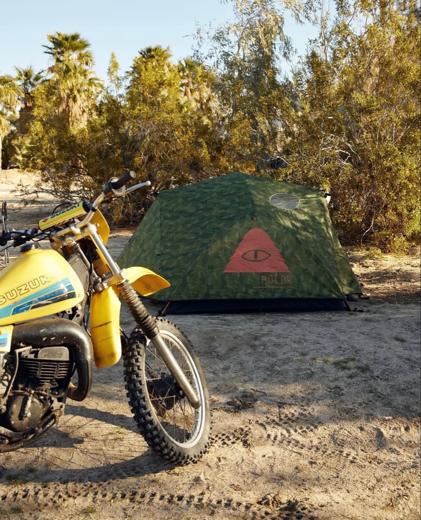 A dark tent is pitched on a forest floor with tall trees and a van in the background.