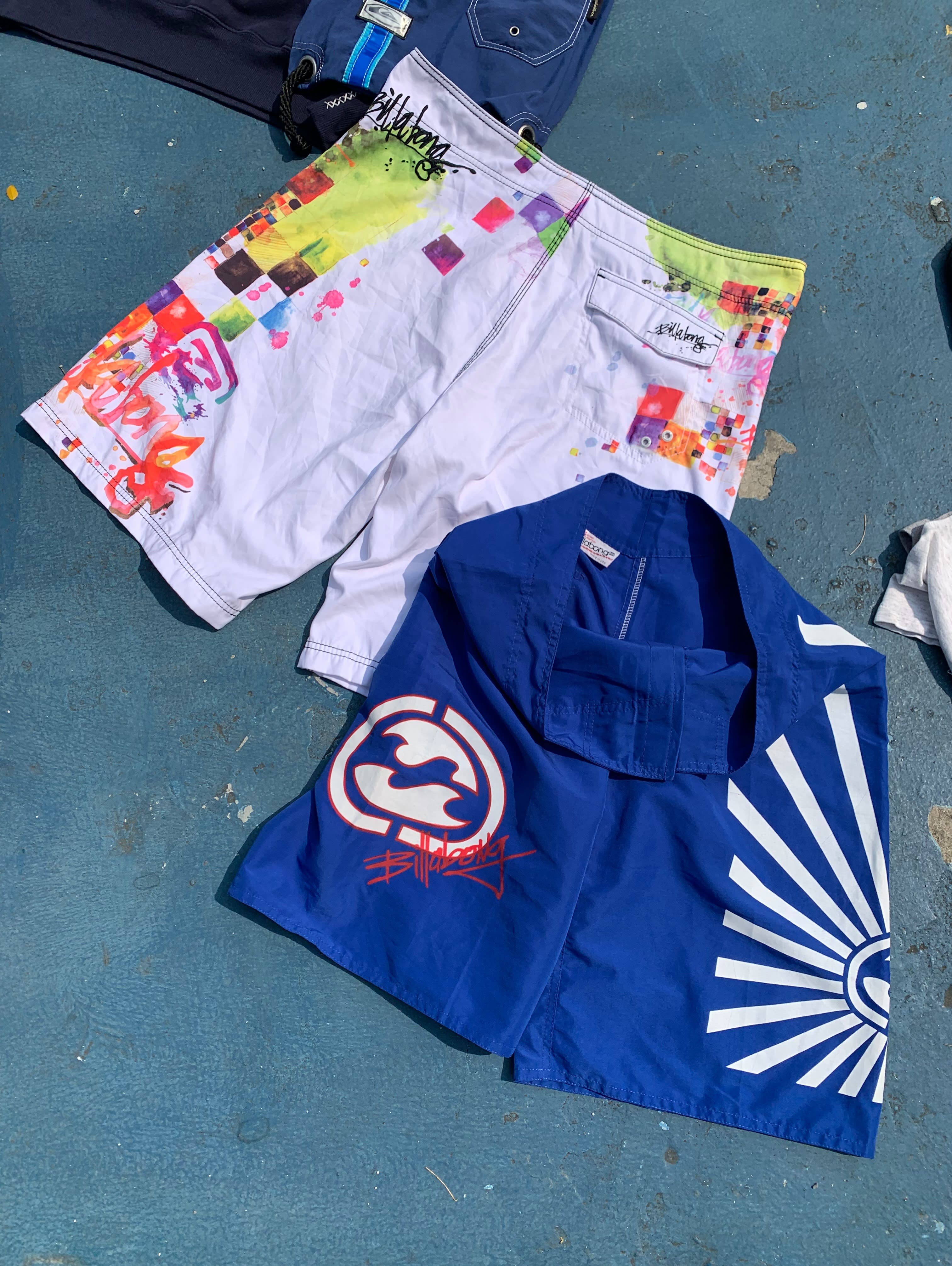 A blue patterned shirt and colorful white shorts lie on a blue textured surface.