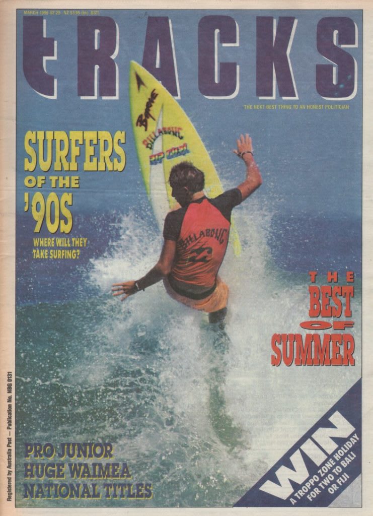 A surfer carrying a yellow surfboard walks into the ocean waves under a large "TRACKS" magazine title.
