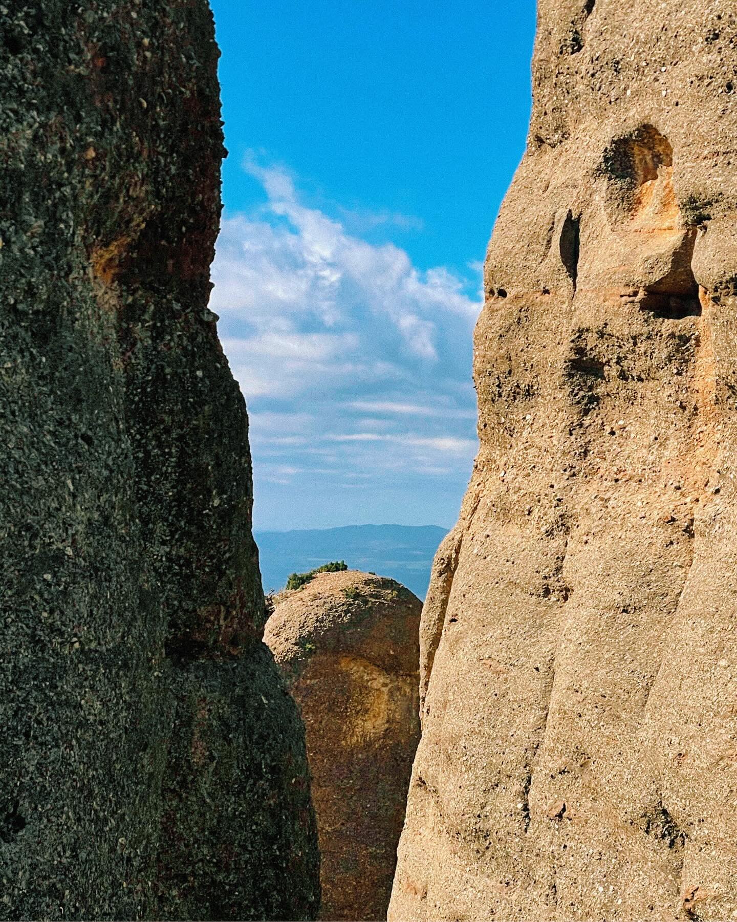 Two large, textured rock formations frame a view of a distant blue mountain range under a bright, cloudy sky.